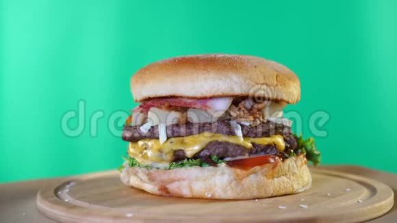 新鲜多汁的汉堡奶酪酱汁和蔬菜在绿色屏幕背景前的木板上旋转视频的预览图