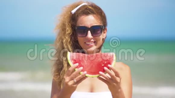 微笑的女人在海滩上吃西瓜女人吃美味的夏天水果暑假快乐视频的预览图