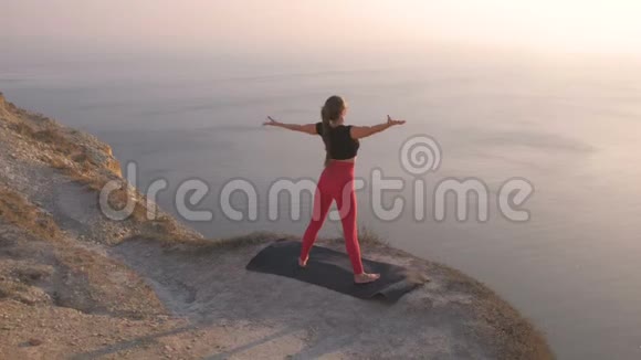 美丽的景色女人做瑜伽伸展在山上日落时的海景伸展手臂视频的预览图
