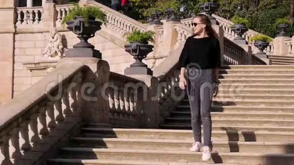 戴着太阳镜的青少年走下楼梯散步的晴朗天气古老建筑的长镜头肖像视频的预览图