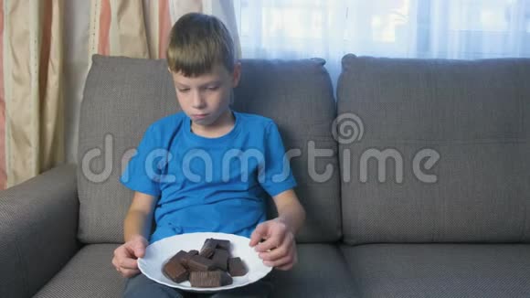 十几岁的男孩坐在沙发上吃巧克力糖果不健康饮食观念视频的预览图