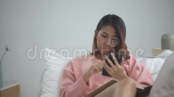 在家学习的年轻亚裔女性躺在家里的沙发上在手机上看短信或短信视频的预览图