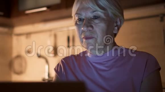 高级女性晚上在家办公室用笔记本电脑听无线耳机音乐视频的预览图