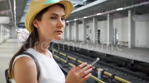 地上地铁站的年轻女子女游客在等候火车时使用手机视频的预览图