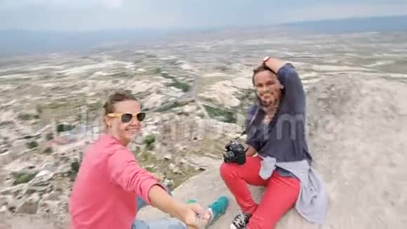 两个年轻的女旅行者坐在山的边缘自拍视频的预览图