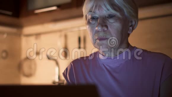 高级妇女在使用笔记本电脑时从玻璃中喝水家庭办公室夜班自由职业者视频的预览图