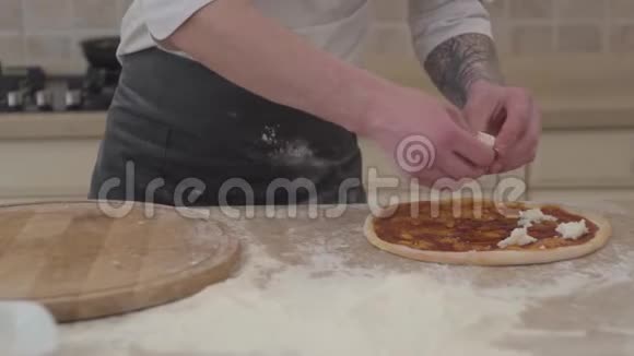 一个面目全非的男人把奶酪放在他的披萨基地厨师手加奶酪比萨饼面团视频的预览图