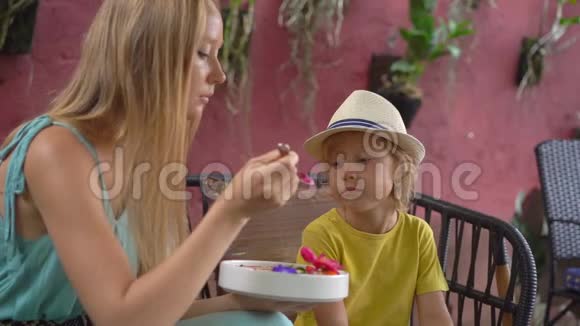 年轻的女人和她的小儿子坐在一家漂亮的咖啡馆里享受着碗里五颜六色的麦片粥健康饮食视频的预览图