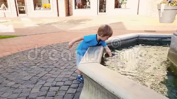 4k视频可爱的幼儿男孩在公园的喷泉里摸水视频的预览图