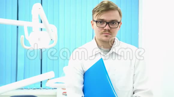一位年轻的男医生站在医疗办公室手臂下拿着一个蓝色文件夹的肖像医学概念视频的预览图
