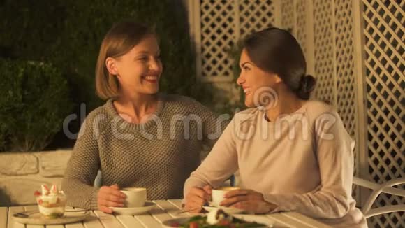 快乐的女士拥抱最好的朋友坐在咖啡馆的露台上愉快地交谈视频的预览图