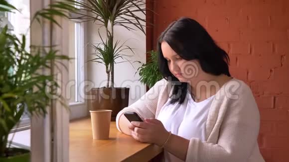 帕菲白种人女孩在桌上的智能手机上滚动和打字在咖啡馆里喝着一杯饮料视频的预览图