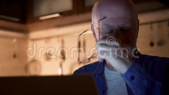 老人晚上在家里办公室用笔记本电脑工作商人摘下眼镜揉揉眼睛视频的预览图