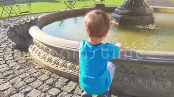4k视频可爱的幼儿男孩在公园的喷泉里摸水视频的预览图