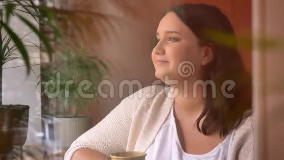 超重的白种人妇女在镜头中微笑在室内端着咖啡的肖像视频的预览图