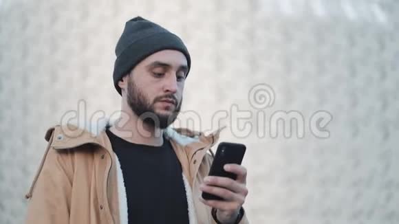 在户外用手机发送音频信息的人他穿着一件秋日夹克和一顶针织帽子在线交流视频的预览图