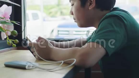 亚洲小男孩在咖啡馆的触摸板上享受游戏视频的预览图