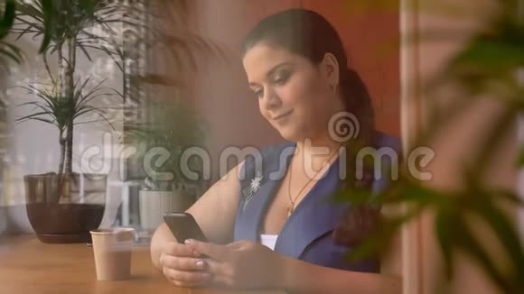 厚厚的白种人女人拿着她的计划一边在窗边喝咖啡一边滚动着视频的预览图