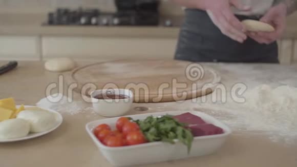 穿着厨师制服的年轻比萨饼师把面团扔在厨房里披萨上的配料视频的预览图