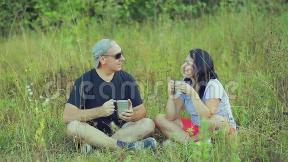 欢乐的男女游客坐在草地上喝着杯子里的茶聊天视频的预览图