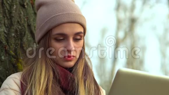 迷人的年轻女孩在公园里带着笔记本电脑喝咖啡从侧面看视频的预览图