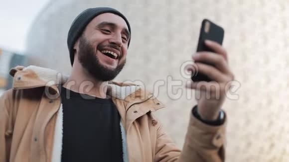 快乐的年轻胡须男有视频聊天拿着智能手机摄像头和朋友聊天外部视频的预览图