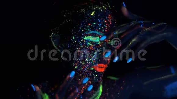 女孩用荧光化妆身体艺术设计在紫外线彩绘的脸五颜六色的化妆霓虹灯中女孩的肖像视频的预览图