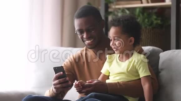 快乐的非洲爸爸和小儿子笑着看着电话视频的预览图