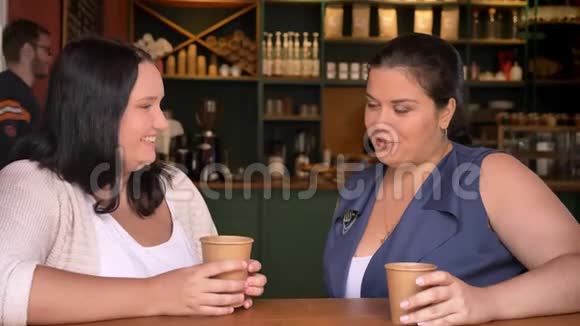 两个肥胖的白种人女孩在桌上的咖啡馆里喝咖啡聊天视频的预览图