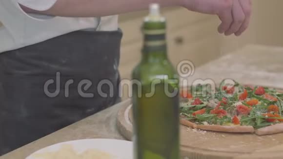 一个面目全非的男人把磨碎的奶酪放在他的披萨基地食品准备的概念带橄榄的瓶子视频的预览图