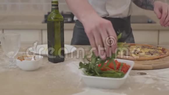 一个面目全非的男人的双手把阿鲁古拉放在他的披萨顶部躺在桌子上食物概念视频的预览图