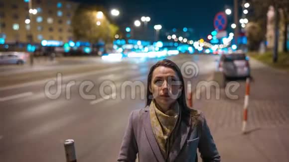 女人静静地站在拥挤的晚街上模糊的快速移动的汽车在她身后移动视频的预览图