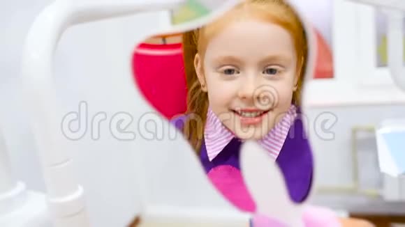 一个红头发的小可爱女孩在坐在牙科椅上的镜子里欣赏她健康的牙齿视频的预览图