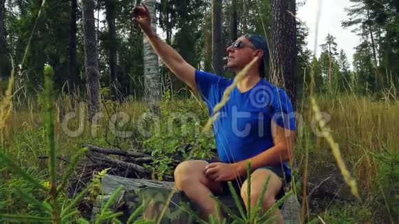 阳光明媚的一天一位戴着太阳镜和棒球帽的男性游客坐在一棵倒下的树上带着一顶棒球帽视频的预览图