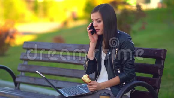 迷人的年轻女孩吃着面包在笔记本电脑上工作在电话里交谈视频的预览图