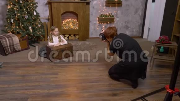 摄影师在圣诞树和壁炉背景上为少女拍照视频的预览图