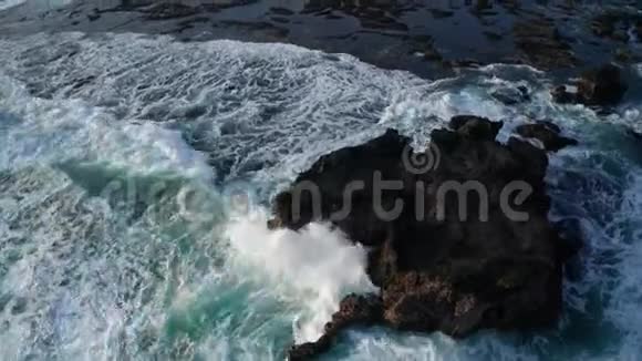 鸟瞰美丽的海浪在巴厘岛黑色沙滩上的岩石上破碎视频的预览图