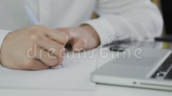 商人使用笔记本电脑并在记事本上写下信息的宏观镜头视频的预览图