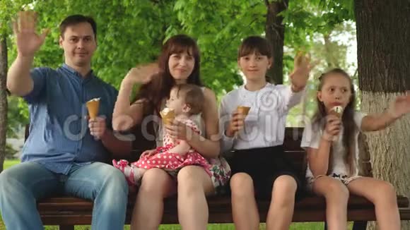 爸爸妈妈和女儿吃冰淇淋笑着挥手大家庭正在公园的长凳上休息周末与视频的预览图