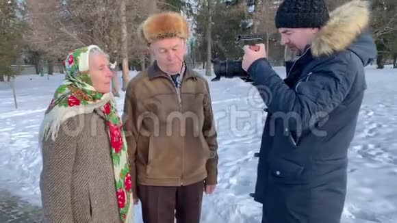 电影制作人与老年夫妇散步并制作视频冬天浪漫的高级情侣在公园散步视频的预览图