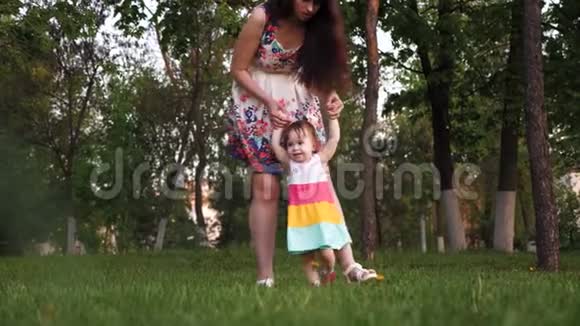 妈妈和她的小女儿在公园的绿草上散步妈妈在公园里和宝宝玩散步微笑着视频的预览图