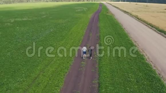 一个年轻人和一个女孩沿着绿色和谷物田旁边的土路慢跑视频的预览图