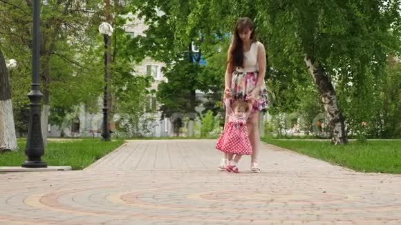 快乐的宝宝在做他的第一步让妈妈的手在绿色公园散步在白天视频的预览图