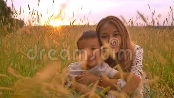 亚洲母亲温柔地抱着她的男孩她在麦田的夕阳下伸出拇指快乐地微笑着视频的预览图