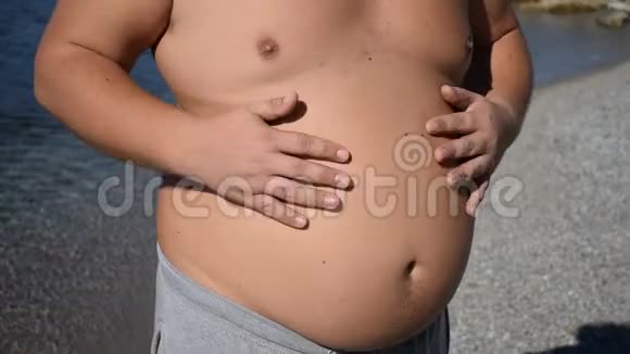 丰满的男人抚摸着他站在海洋上的腹部超重和健康问题视频的预览图