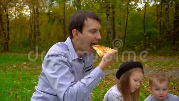 爸爸咬披萨在公园草坪上野餐视频的预览图