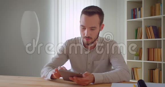 年轻英俊的白种人商人用平板电脑在公寓里看着照相机的特写肖像视频的预览图