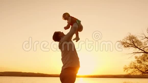 爸爸在日落时和他的女儿玩用手把他的小女儿高高地举到天空慢动作视频的预览图
