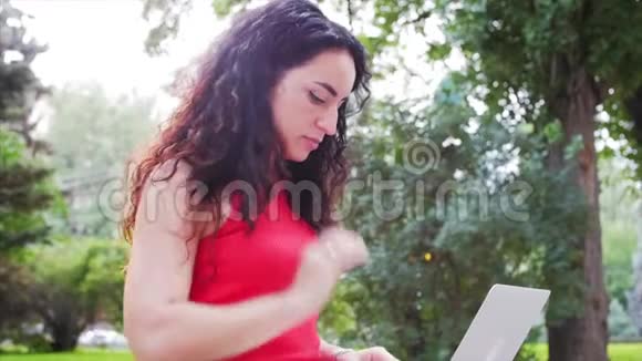 在笔记本电脑上工作的女人穿着黑色短裤的漂亮的布鲁内特在公园里做着笔记本电脑的工作女孩在她的身上打印出来视频的预览图
