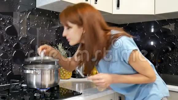 快乐的黑发女人站在厨房的炉子旁用平底锅做饭闻到饭菜的香味视频的预览图